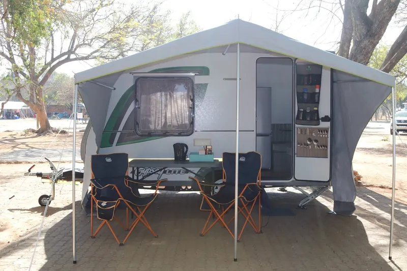 A Gypsey Lite caravan on a campsite with its awning out, a kettle on the table and two camp chairs in the shade