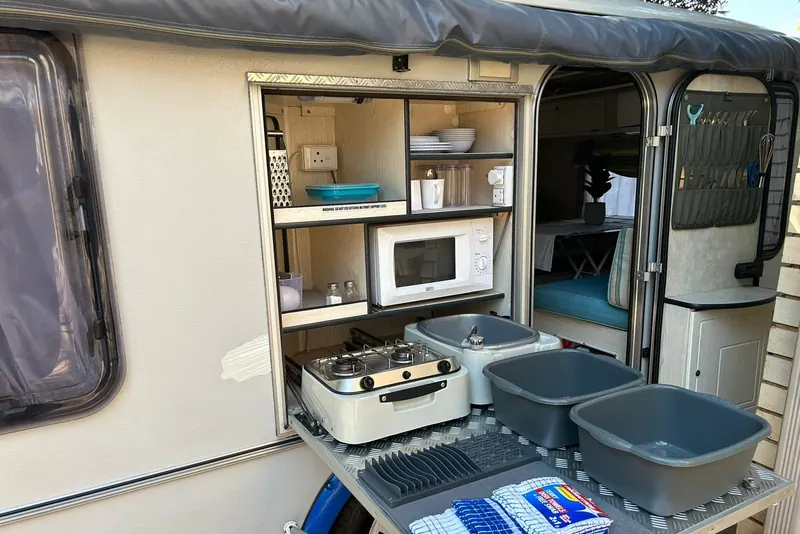 A caravan's outdoor kitchen slid open, showing the gas hob, basins and crockery