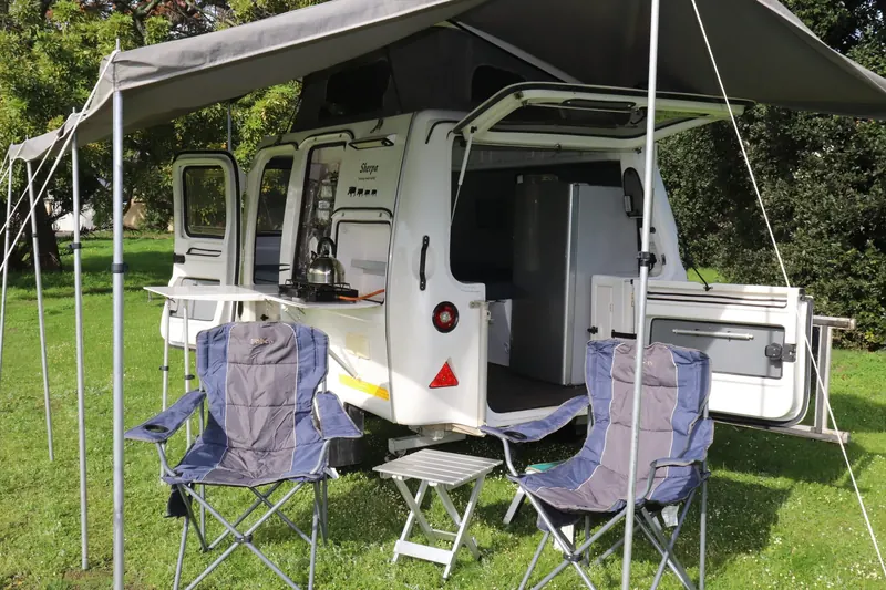 A caravan with its awning, chairs and table still set out on a lawn, ready to be packed away