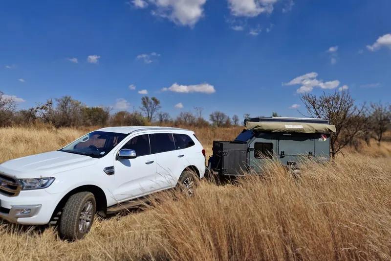 A white Ford Everest hitched to an off-road trailer in long grass under a blue sky